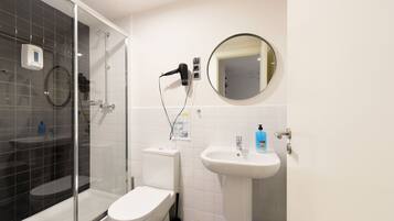 A modern bathroom with a glass-enclosed shower, a toilet, a sink, and a hairdryer on a wall-mounted station.