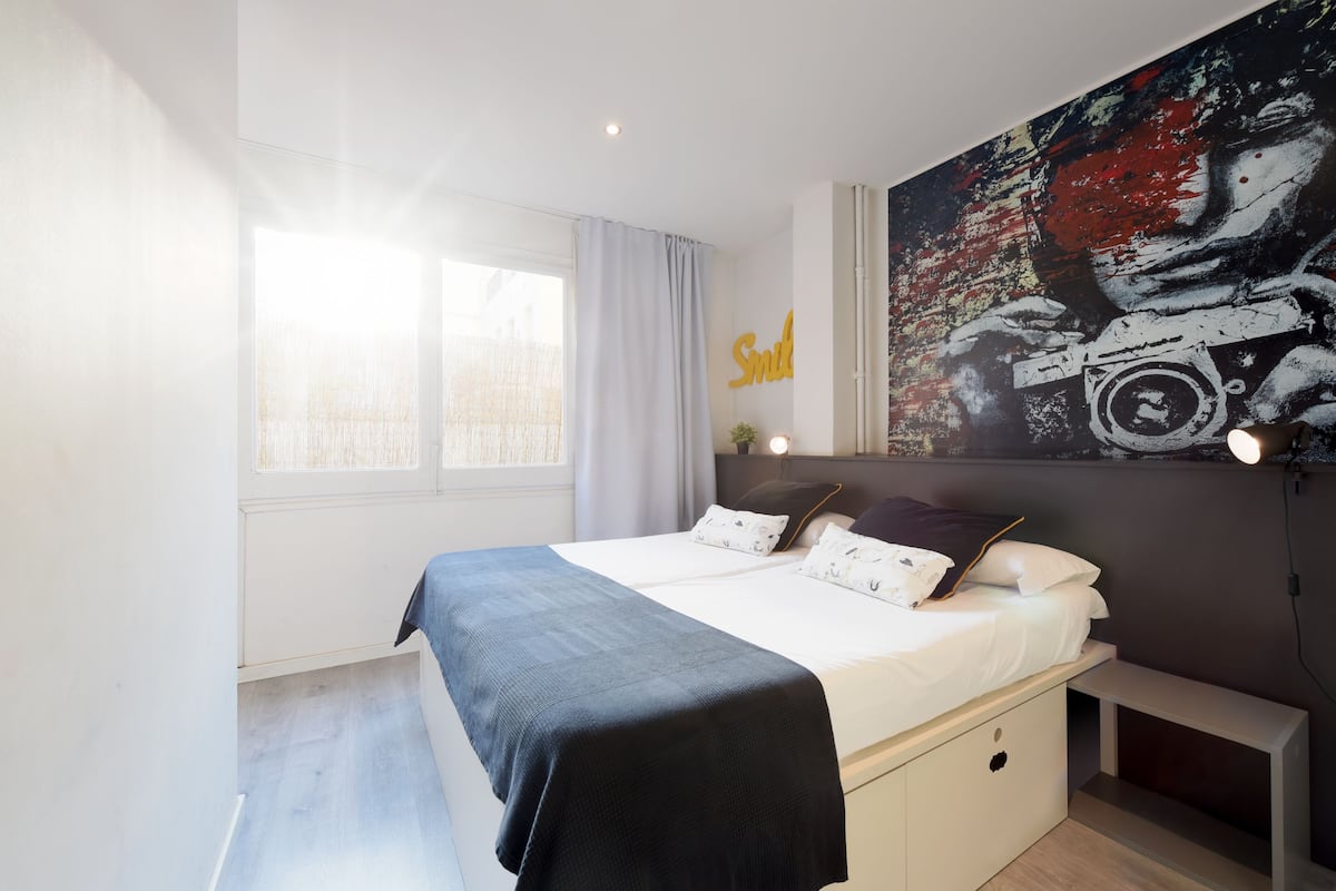 Ein modernes Schlafzimmer mit einem großen Bett, einem Wandbild und einem Fenster mit Vorhängen.