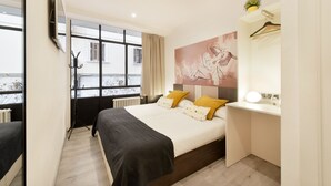 A modern hotel room with a large bed, a desk, a TV mounted on the wall, and a window with a view of buildings. - Free Hostels Barcelona (Barcelona)