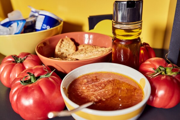 Ett bord med en skål tomatssoppa, en flaska olivolja, en skål med kex och flera tomater.