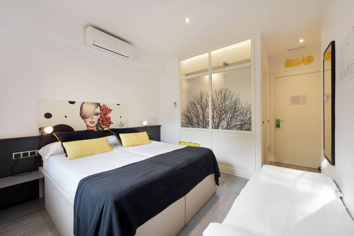 Ein modernes Hotelzimmer mit einem großen Bett, einem Nachttisch, einem Spiegel und einem Schrank mit integriertem Fenster.