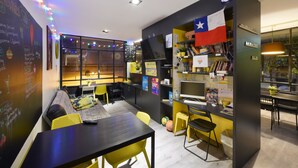 A modern, well-lit room with a blackboard, yellow chairs, a black table, and a bookshelf with various items. - Free Hostels Barcelona (Barcelona)