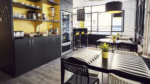 A modern kitchen with dark cabinets, a central island, and a dining area with striped chairs and tables. - Free Hostels Barcelona (Barcelona)