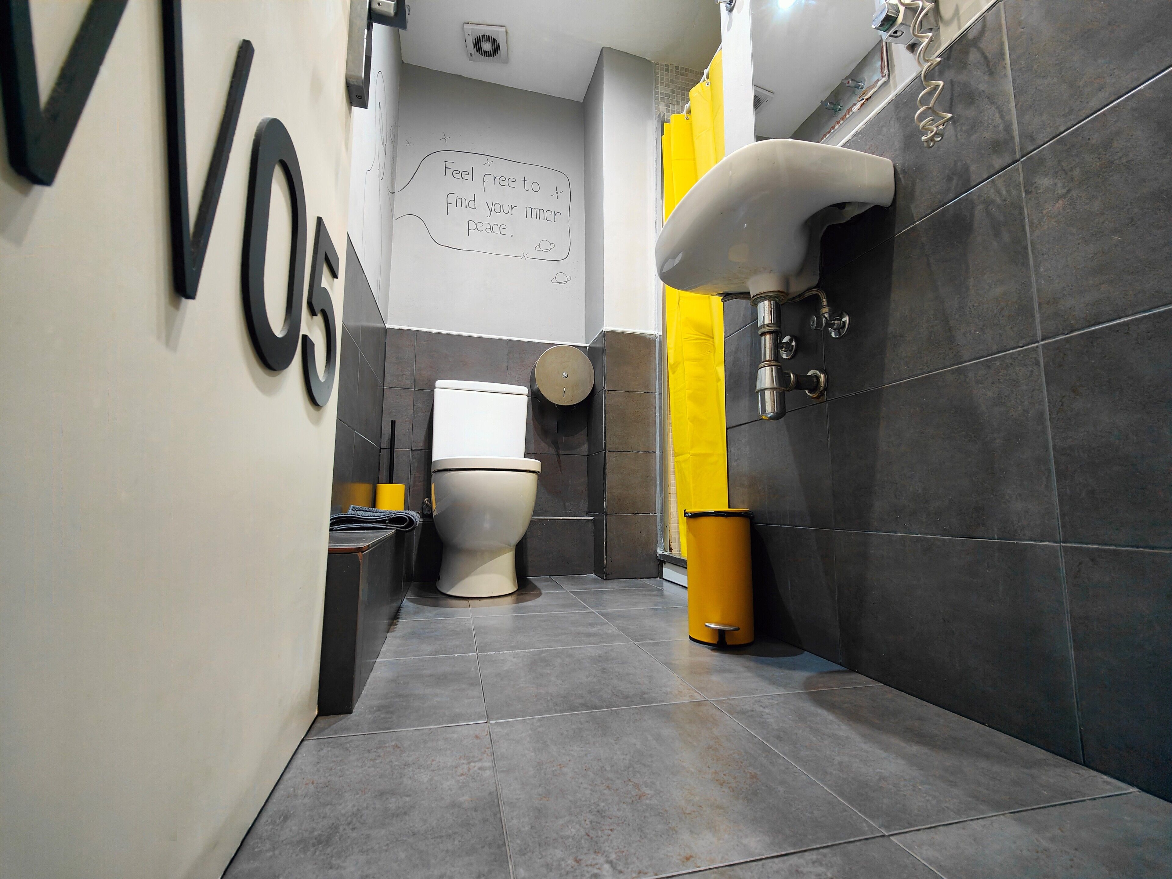 Un baño moderno con inodoro, un cubo de basura amarillo y un lavamanos empotrado en la pared.