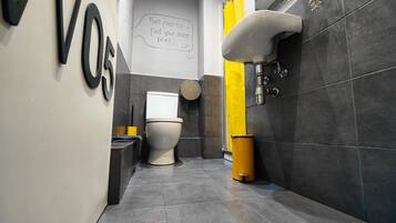 Un baño moderno con inodoro, un cubo de basura amarillo y un lavamanos empotrado en la pared.