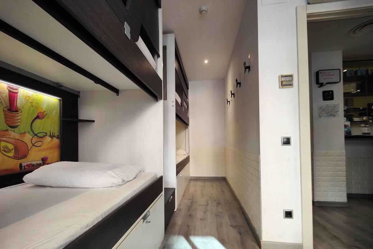 Ein schmaler Korridor mit einem Etagenbett links, einer Küchenzeile rechts und einem Badezimmer im Hintergrund.