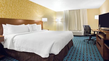 A hotel room with a large bed, a desk with a chair, a television, and a window with curtains.