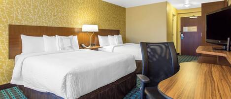 A hotel room with two beds, a desk, a chair, a television, and a patterned carpet.