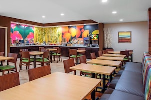 Um restaurante com mesas e cadeiras de madeira, um balcão com um mural colorido e uma área de estar com um sofá.