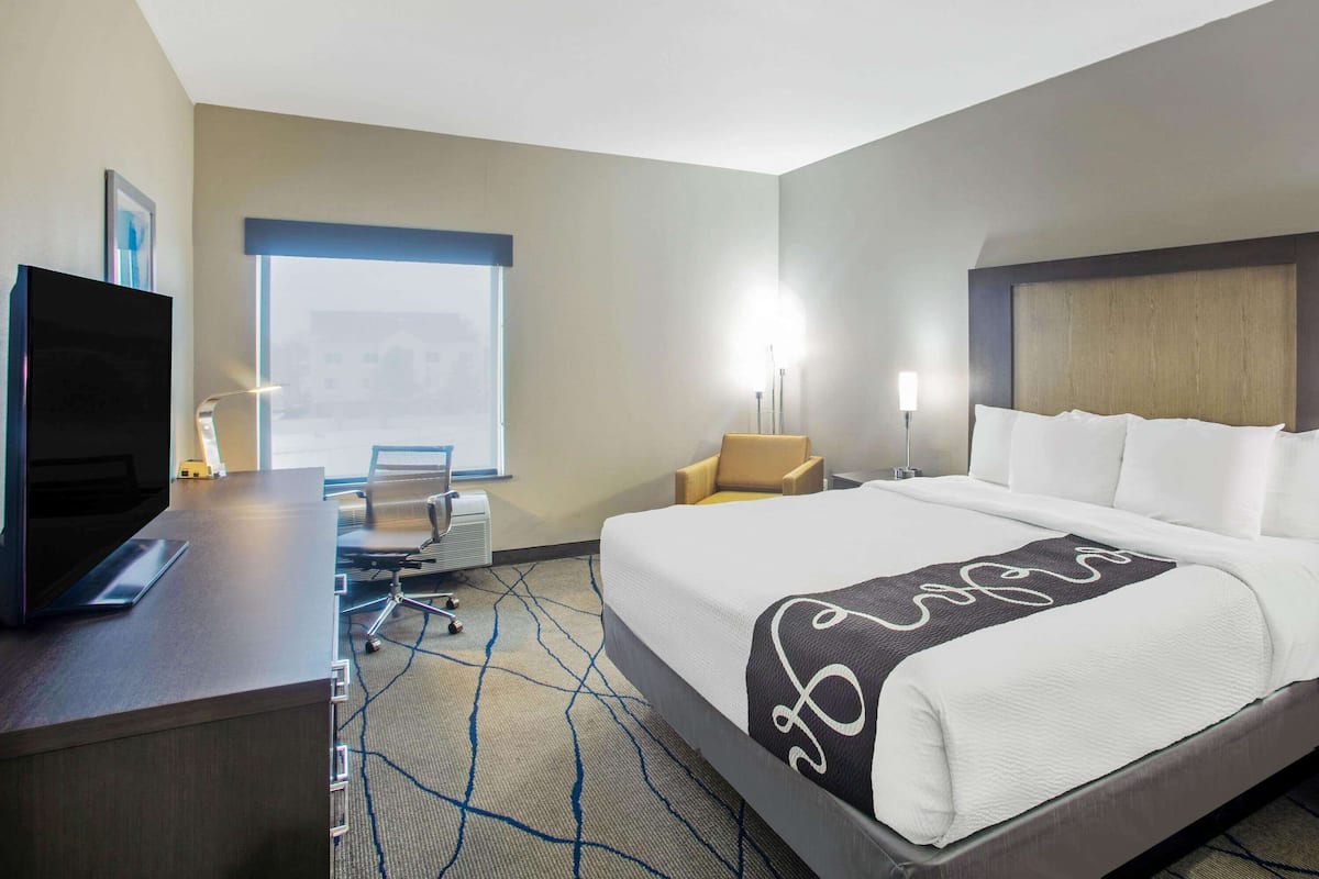 Habitación de hotel con cama, escritorio con ordenador, silla y ventana con vistas a edificios.