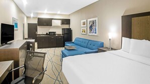 A hotel room with a bed, a desk with a chair, a sofa, a kitchenette, and artwork on the walls. - La Quinta Inn & Suites by Wyndham Ponca City (Ponca City)