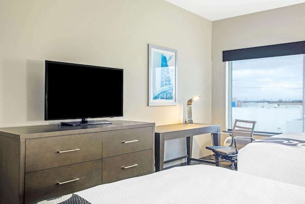 A hotel room with a bed, a desk with a chair, a television on a dresser, and a large window with a view. - La Quinta Inn & Suites by Wyndham Ponca City (Ponca City)