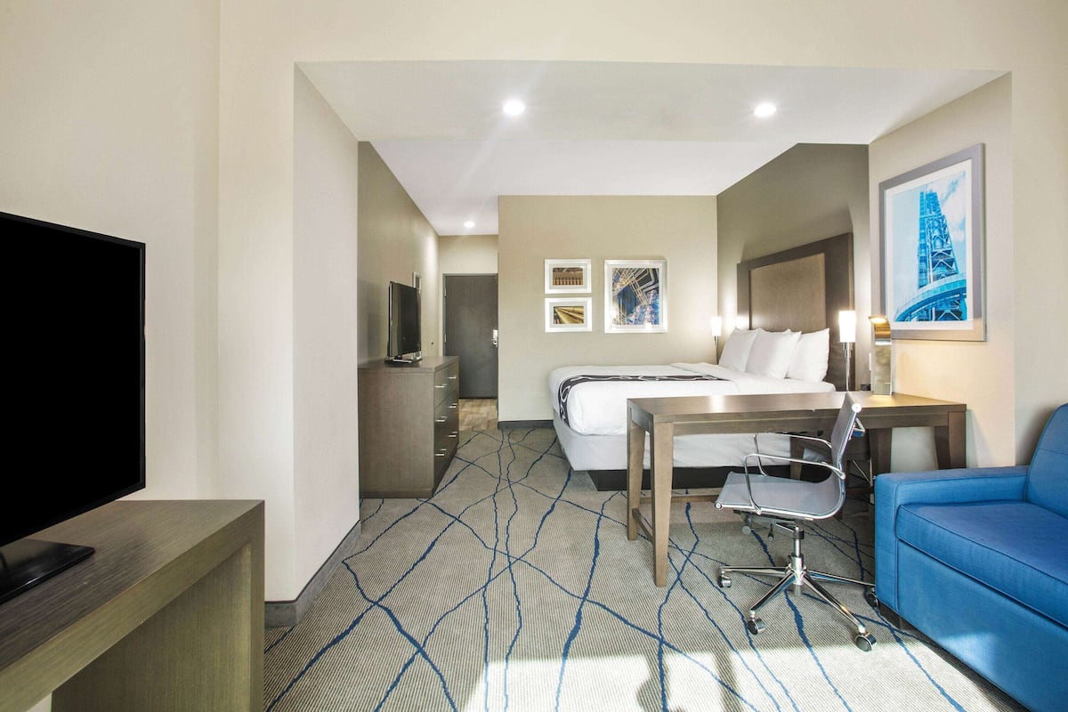 Una habitación de hotel con cama, escritorio, televisor, sofá azul y obras de arte en las paredes.