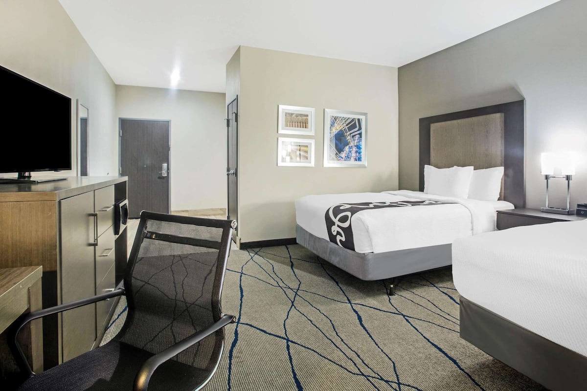 Habitación de hotel con cama, escritorio con televisor, una silla y obras de arte en la pared.