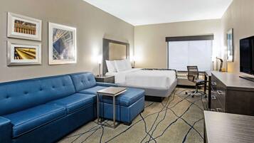 A hotel room with a bed, a blue sofa, a desk, and a TV.