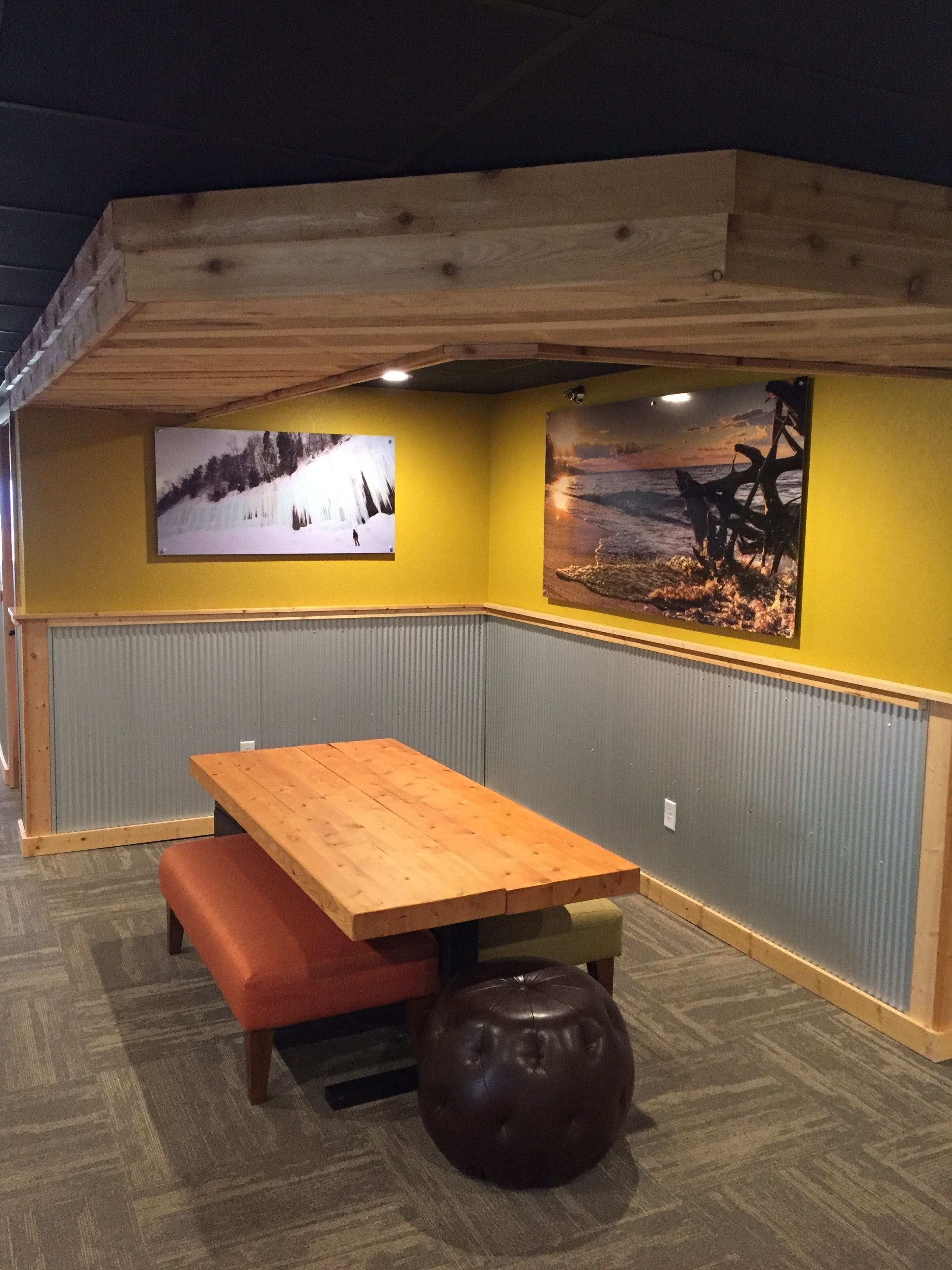 A corner room with a wooden table and bench, two wall-mounted pictures, and a textured floor.
