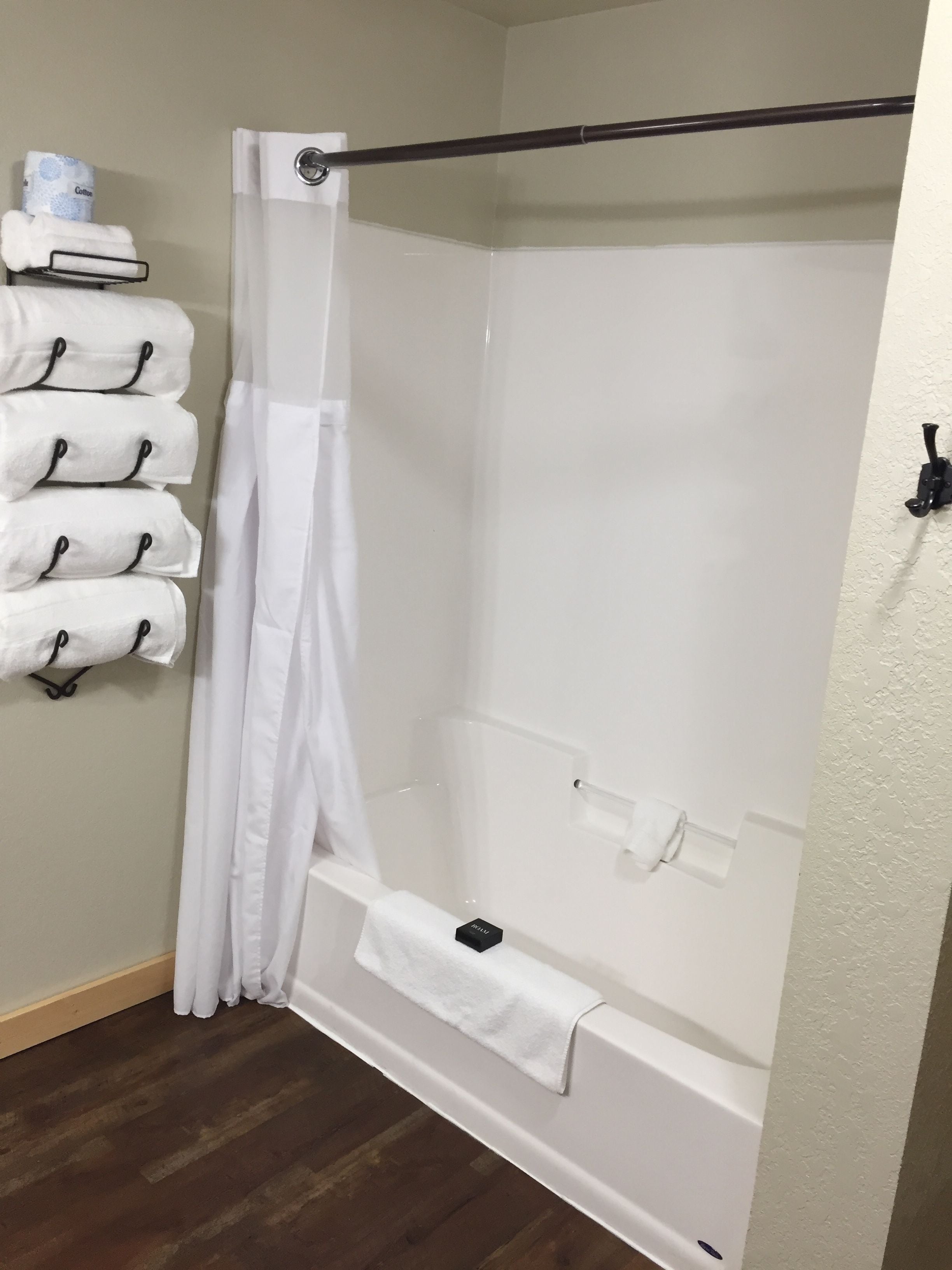 A bathroom with a shower, a towel rack with multiple towels, and a toilet paper holder.