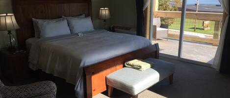 A bedroom with a large bed, two bedside lamps, a bench, and a view of the outdoors.