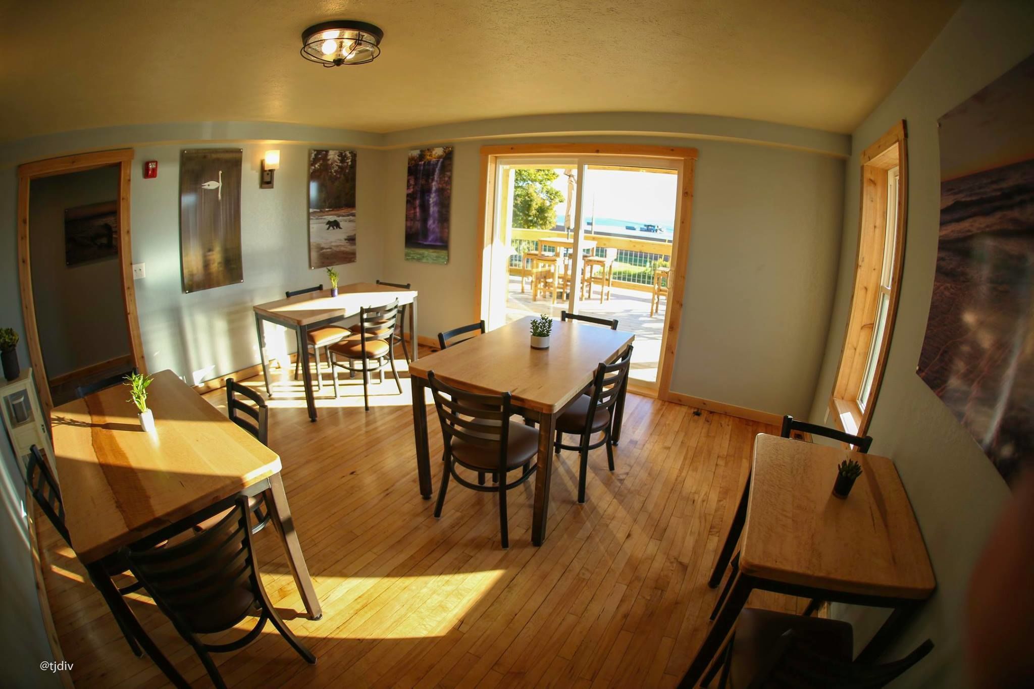 Un comedor con mesas y sillas de madera, una lámpara en el techo y vistas al exterior a través de una puerta corrediza de vidrio.