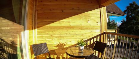 A wooden deck with a glass table and two chairs, a potted plant, and a railing.