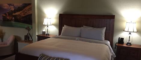 A neatly made bed with a wooden headboard, two bedside lamps, and a small bedside table with a lamp and a camera on it.
