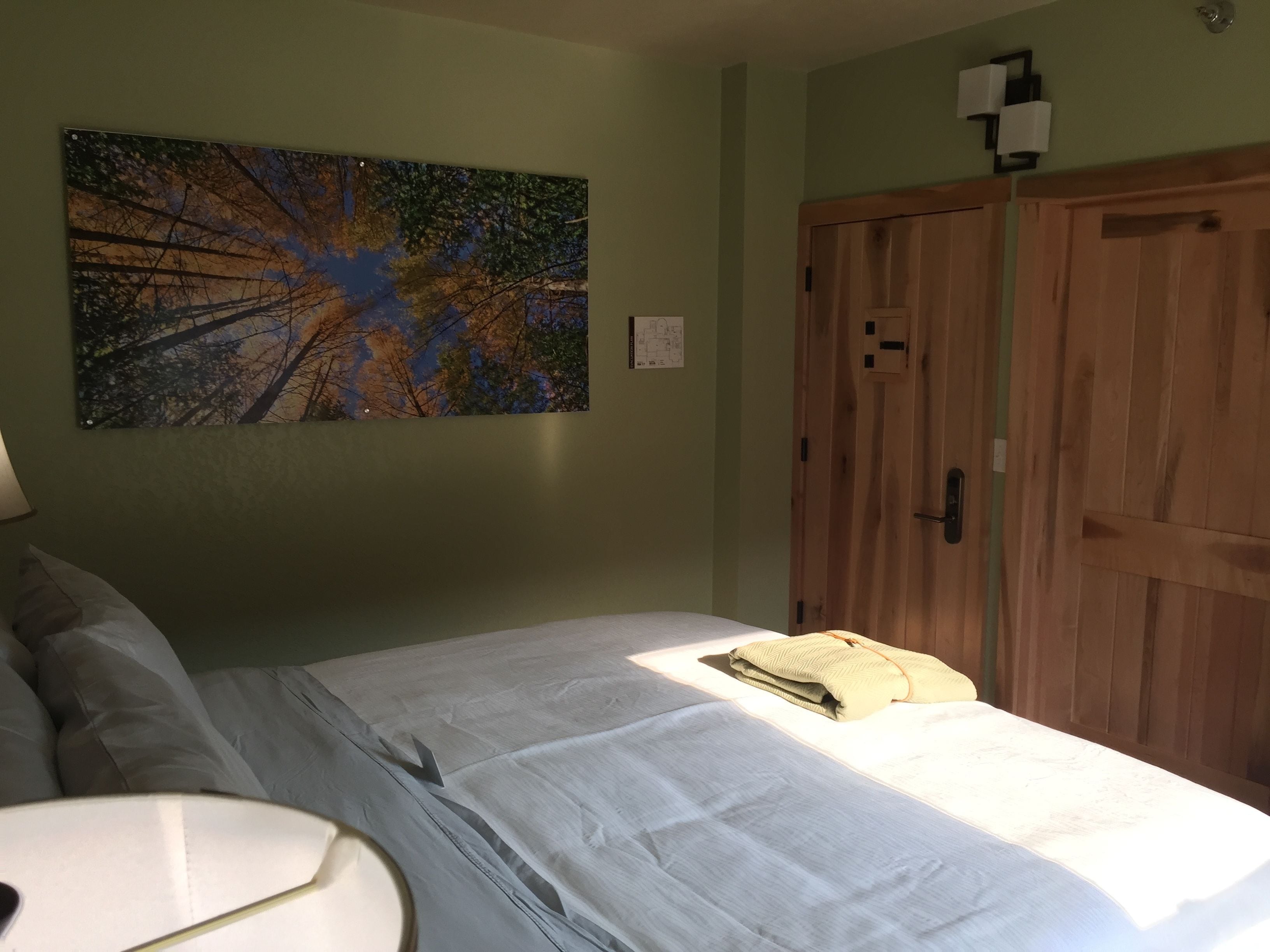 A bedroom with a bed, a nightstand, a painting, and a wooden wardrobe.