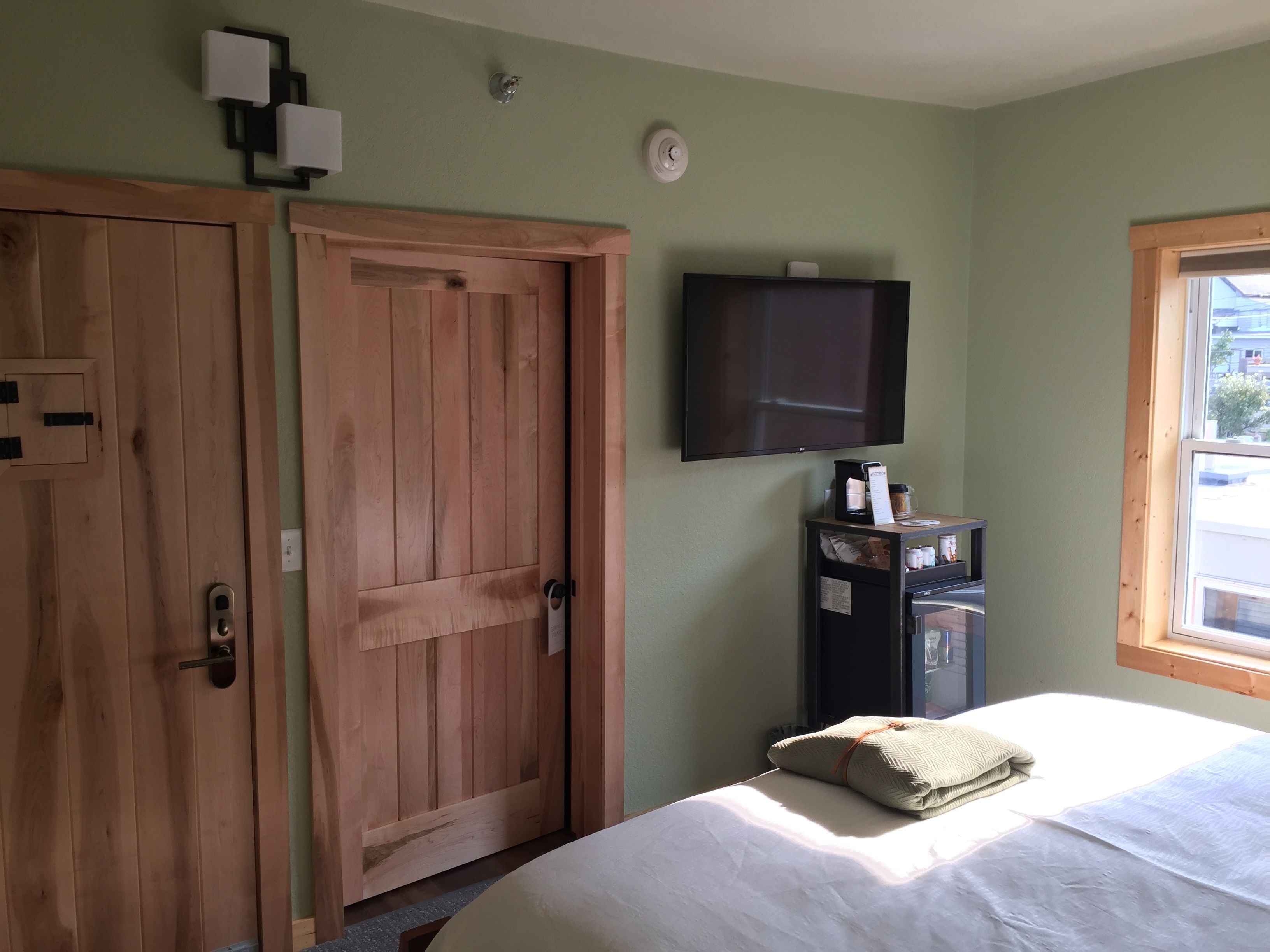 Quarto com uma cama, guarda-roupa de madeira, televisão na parede e uma janela.