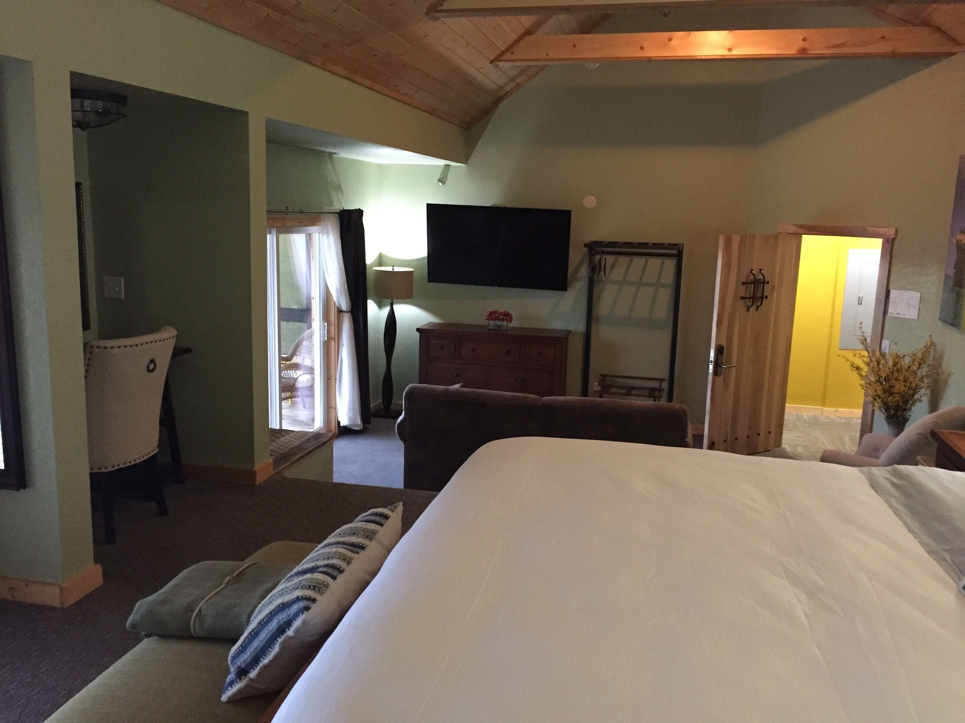 A bedroom with a large bed, a chair, a dresser, a television, and a door leading to another room.