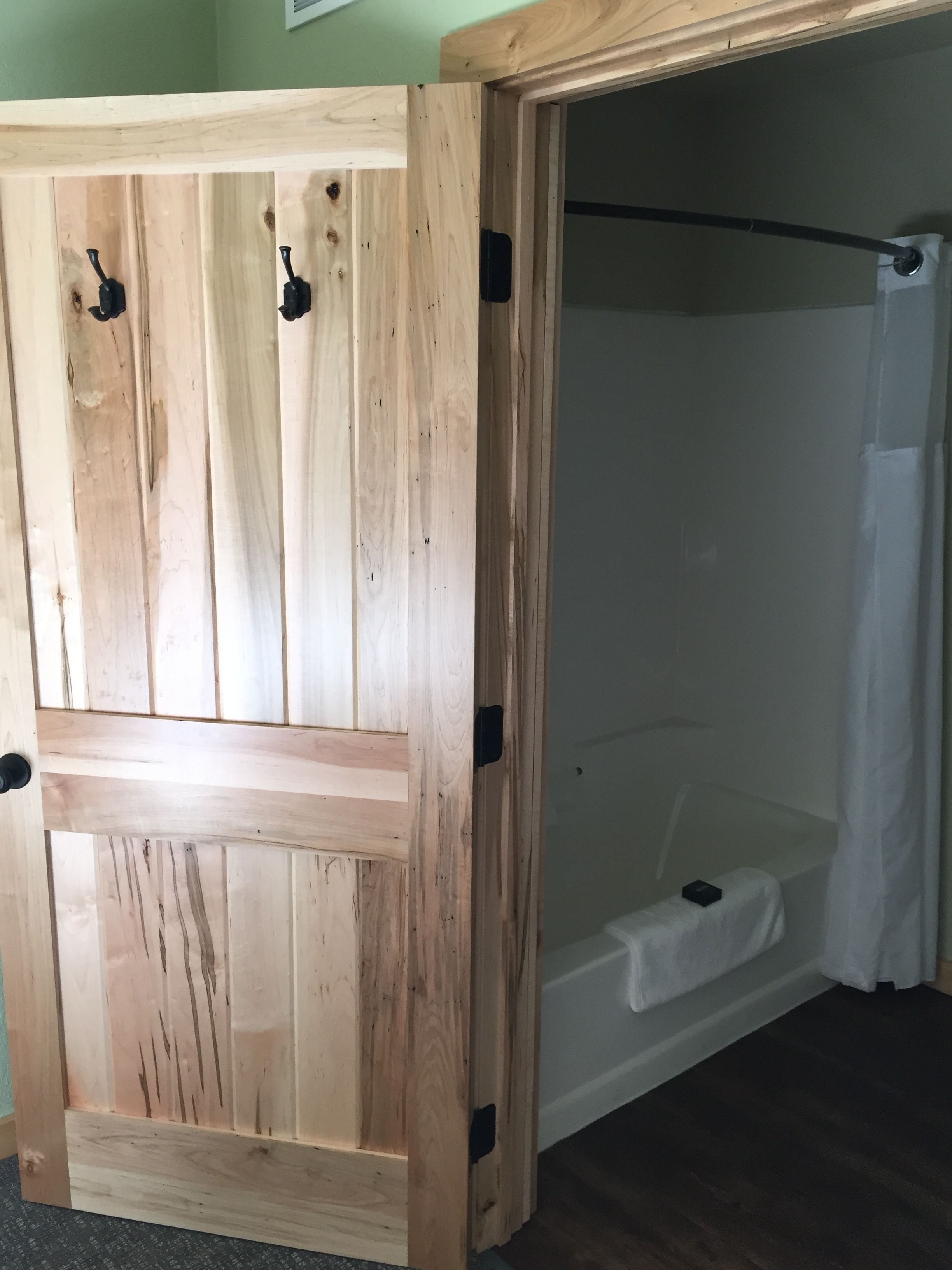 Una puerta de madera con picaporte, que da a un baño con ducha y bañera.