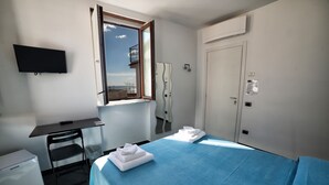 A hotel room with a bed, a desk, a chair, a TV, a window, and a door.