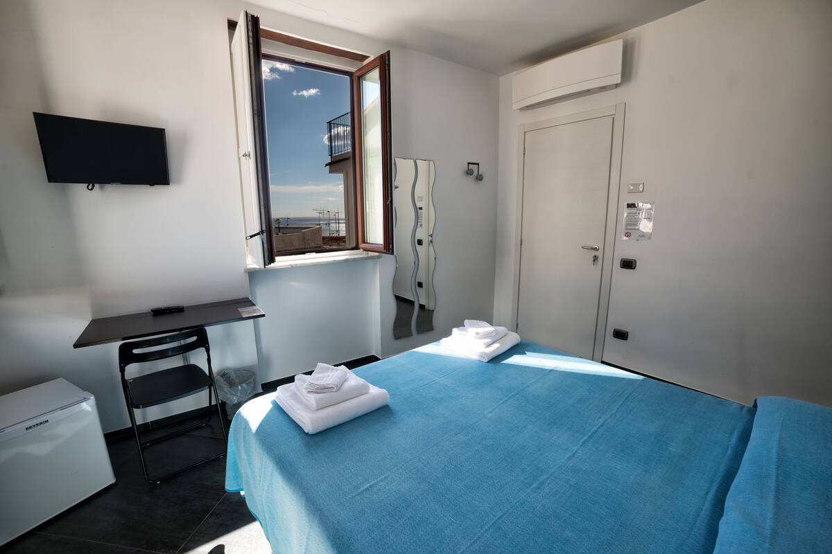 Une chambre d’hôtel avec un lit, un bureau, une chaise, une télévision, une fenêtre et une porte.