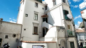A white building with a tiled roof, a balcony with a green railing, and a sign on the wall.