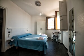 A bedroom with a bed, a desk, a chair, and a window.