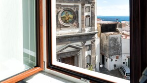 A window with a view of a historic building with a clock, a cross on top, and a clear blue sky.
