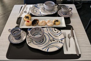 A table set with a plate of assorted cookies, a stack of blue and white patterned cups, and a black placemat.