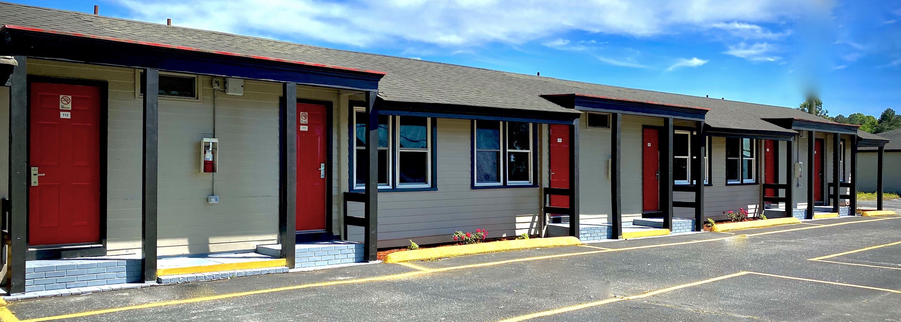 A row of motel rooms with red doors, each with a window and a small porch area.