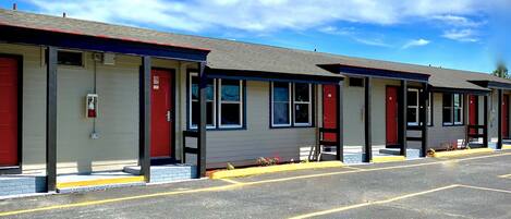 A row of motel rooms with red doors, each with a window and a small porch area.