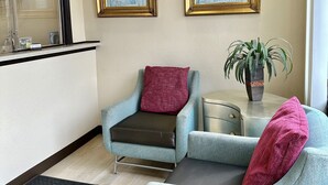 A hotel lobby with two armchairs, a small table with a plant, and two framed artworks on the wall. - Whistling Pines - Daily & Extended Stay, Elizabeth City (Elizabeth City)