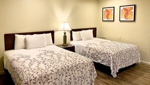 A hotel room with two beds, a nightstand with a lamp, and two framed pictures on the wall. - Whistling Pines - Daily & Extended Stay, Elizabeth City (Elizabeth City)