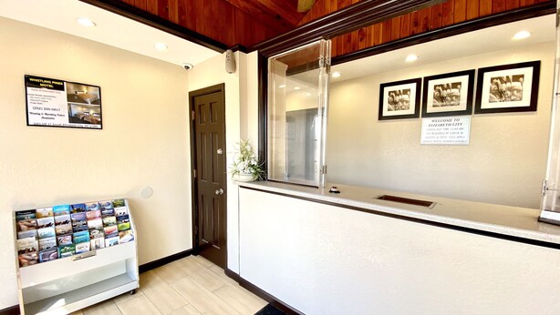 A reception area with a wooden ceiling, a reception desk, framed pictures on the wall, and a display of brochures. - Whistling Pines - Daily & Extended Stay, Elizabeth City (Elizabeth City)