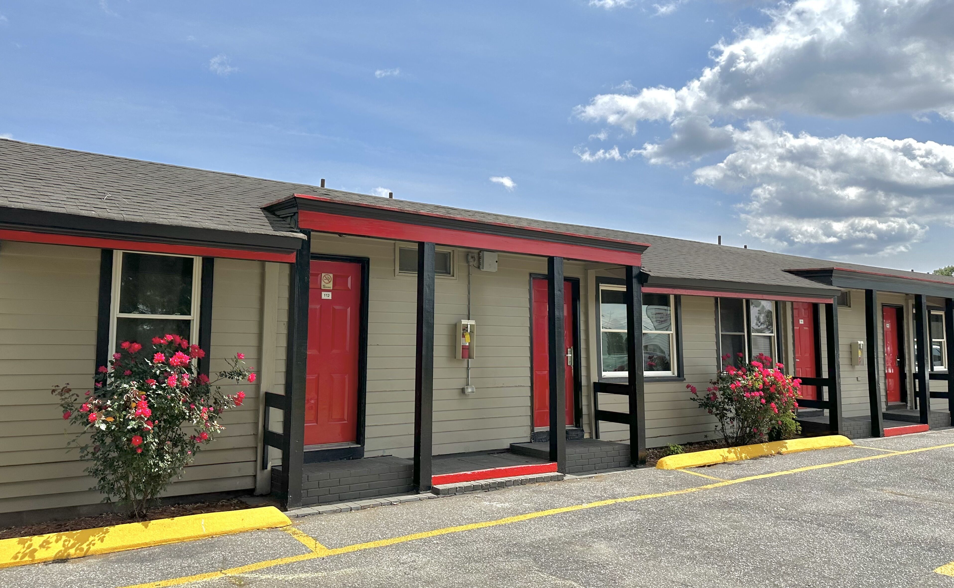 Una hilera de habitaciones de motel con puertas y ventanas rojas, cada una con un pequeño porche y una bordilla amarilla.