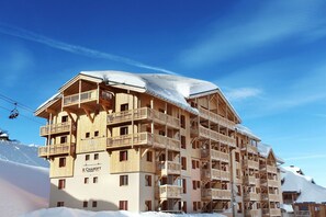 A multi-story wooden building with balconies, a restaurant named 'E Chairift,' and a ski lift in the background.