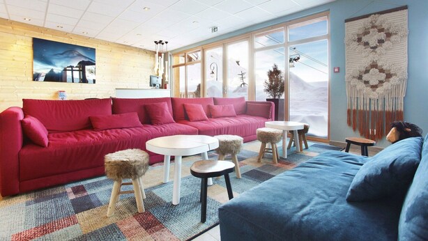 A modern living room with a red sofa, a blue sofa, and a small round table. - Chalet in Paradiski with Pool & Spa (Plagne Villages)