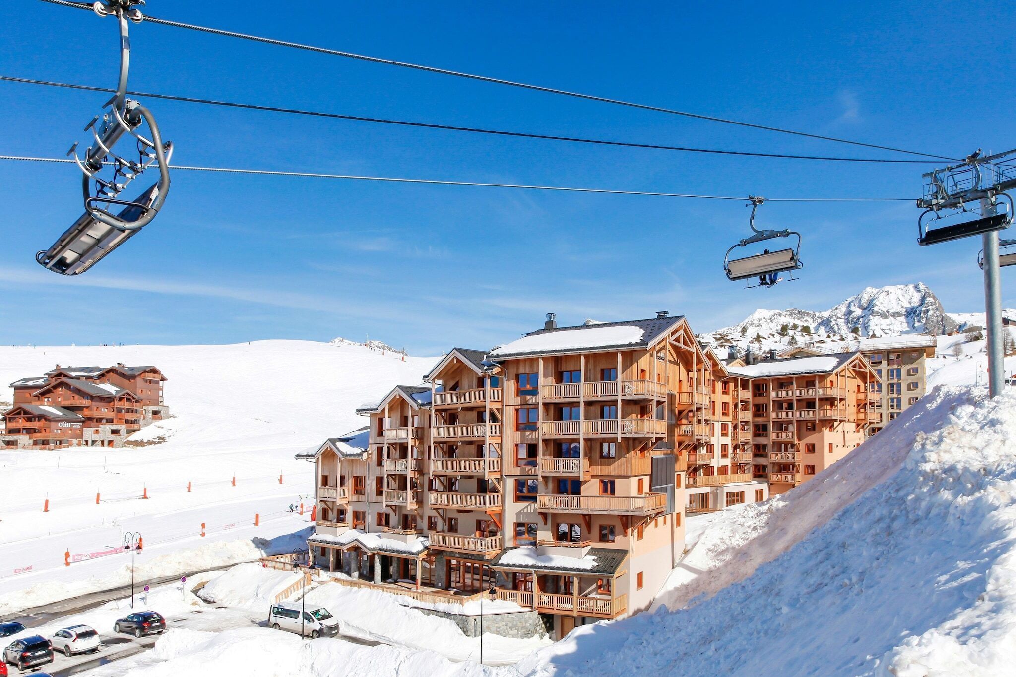 A multi-story wooden building with balconies, ski lift cables, and a snowy mountain backdrop.