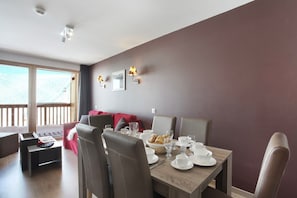 A dining area with a table set for four, chairs, and a window with a view. - Chalet in Paradiski with Pool & Spa (Plagne Villages)