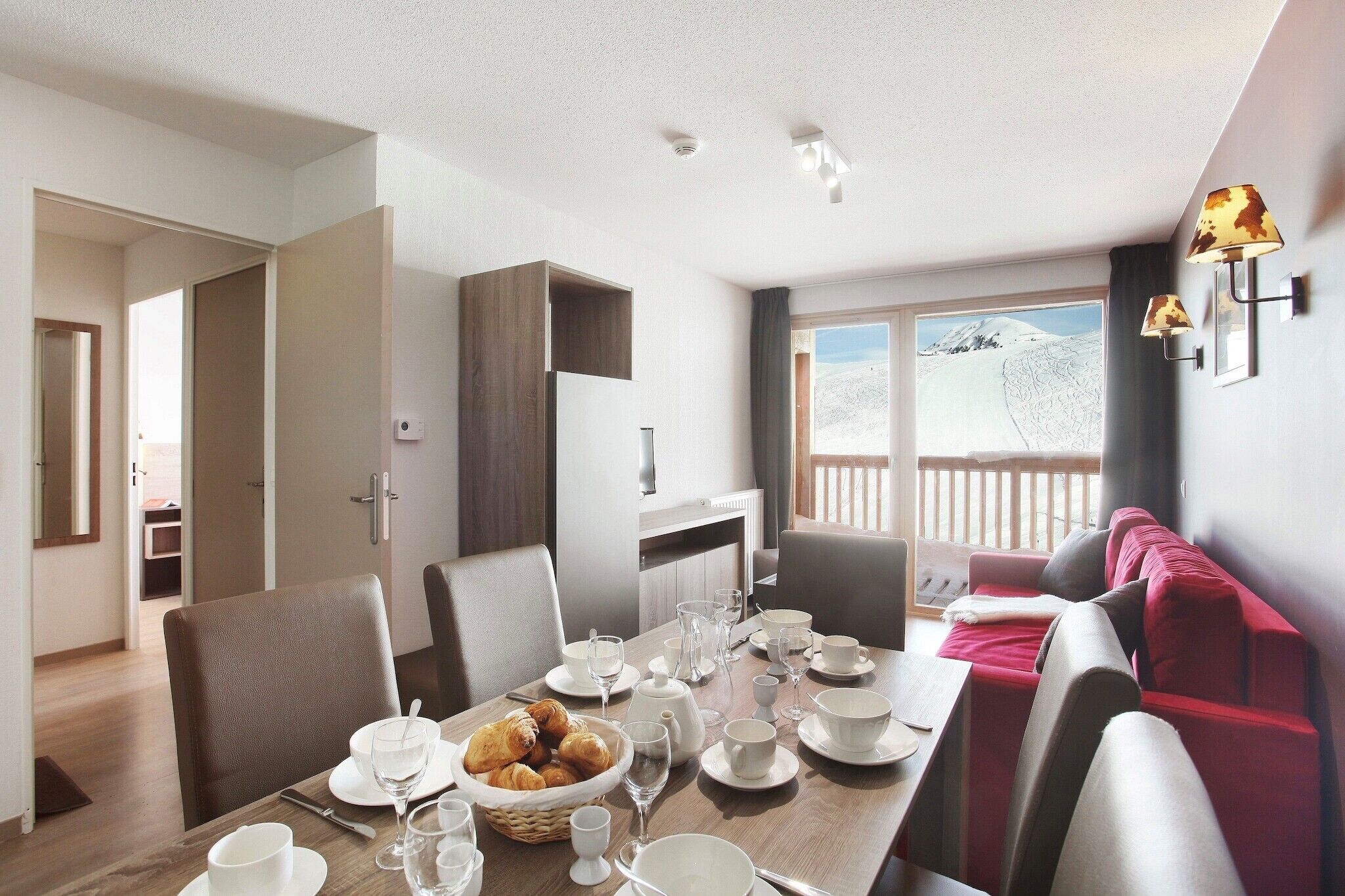 Un coin repas avec une table dressée pour quatre personnes, un canapé et une vue sur un paysage enneigé par de grandes fenêtres.