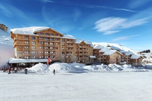 A snow-covered ski resort with multi-story wooden buildings, ski lifts, and a clear blue sky. - Chalet in Paradiski with Pool & Spa (Plagne Villages)