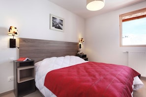 A bedroom with a bed, a nightstand, a lamp, a teddy bear, a framed picture, and a window with a view. - Chalet in Paradiski with Pool & Spa (Plagne Villages)