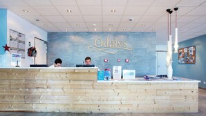 A reception desk with a wooden finish, a wall with the name 'Odalys' in cursive, and a bulletin board with various notices. - Chalet in Paradiski with Pool & Spa (Plagne Villages)
