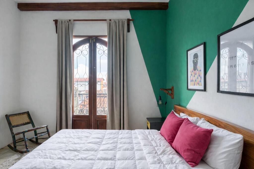 A bedroom with a bed, a rocking chair, a window with curtains, and a green wall.